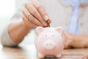 close up of senior woman hand putting coin into piggy bank